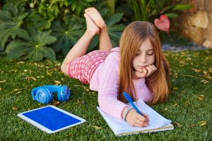 Canva Blond Kid Girl Homework Lying On Grass Turf 300x200
