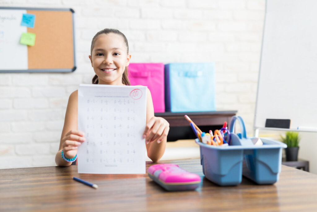 Smiling School Girl Showing Perfect Test Result At Table